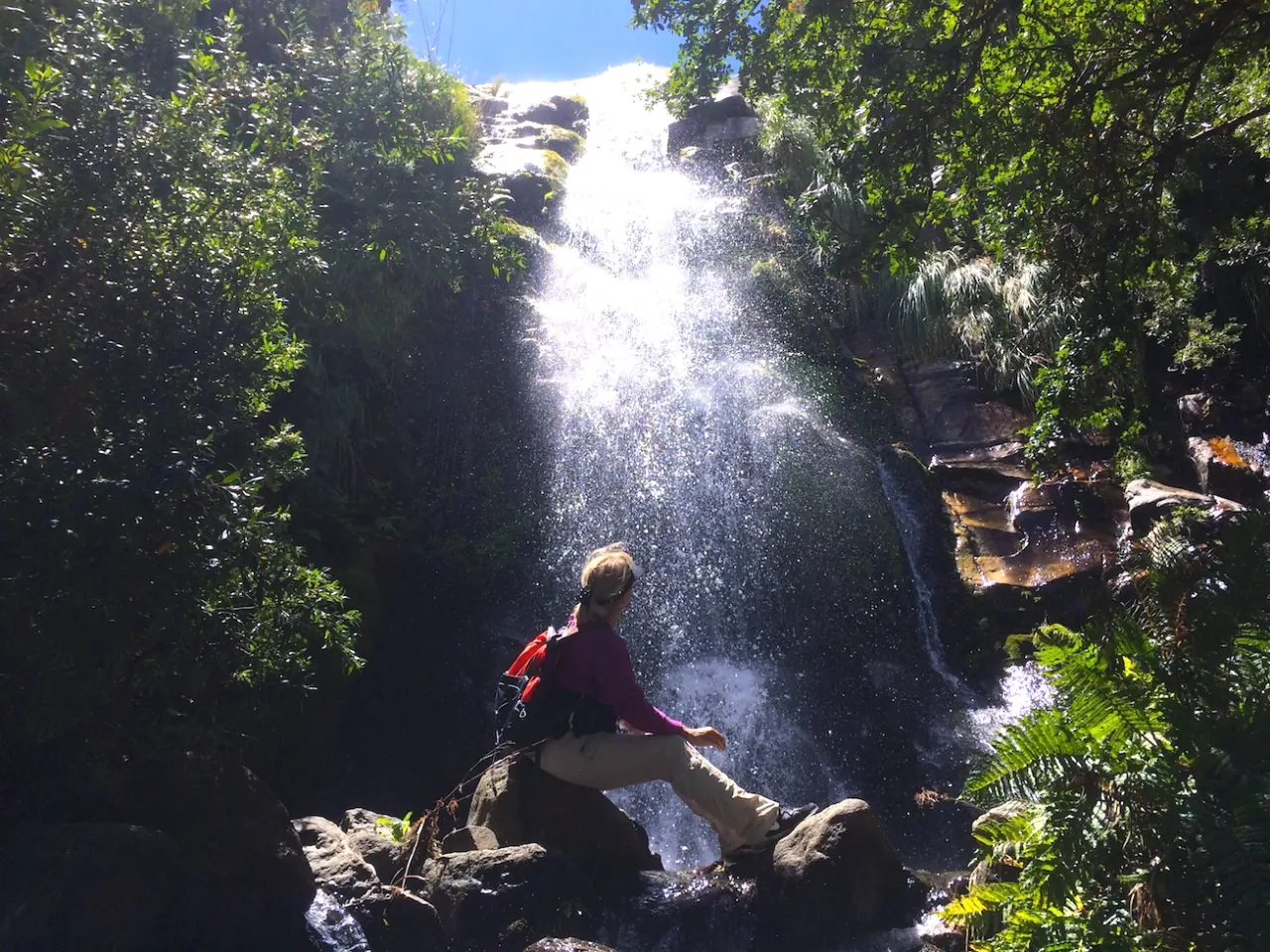 Una persona sentada sobre una roca frente a la cascada.