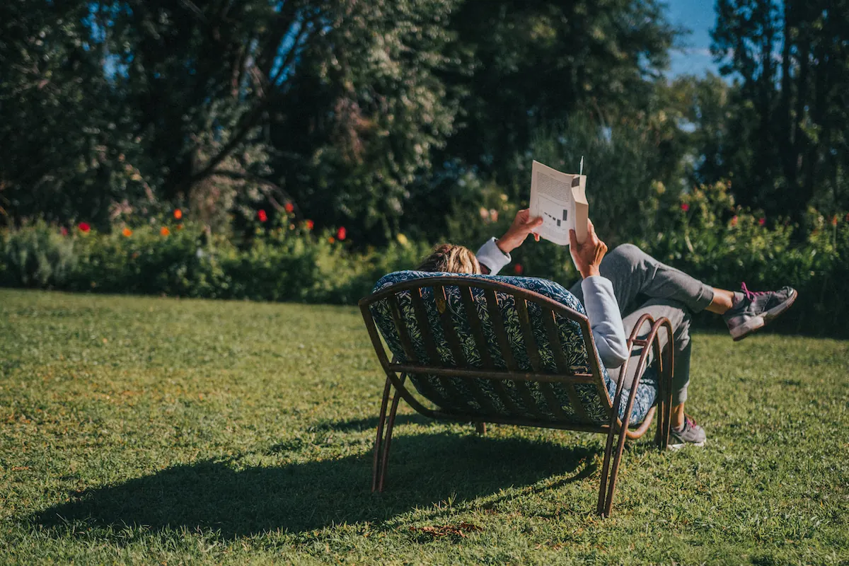 Una persona leyendo tumbada en un banco del parque, al sol de la tarde.