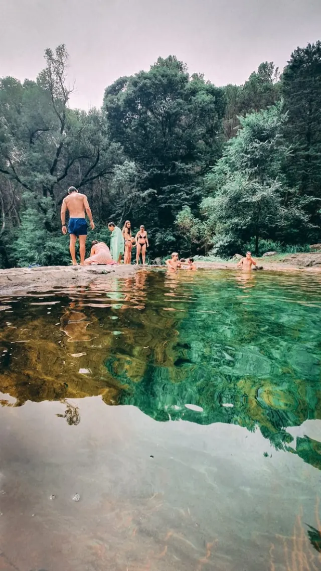 Una olla del arroyo de agua verde y transparente, con gente entrando desde las rocas.