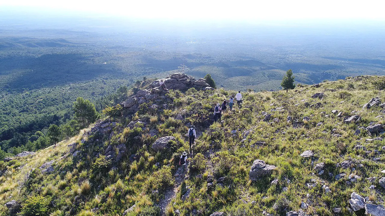 Gente caminando por el filo de la sierra, con el valle abajo.