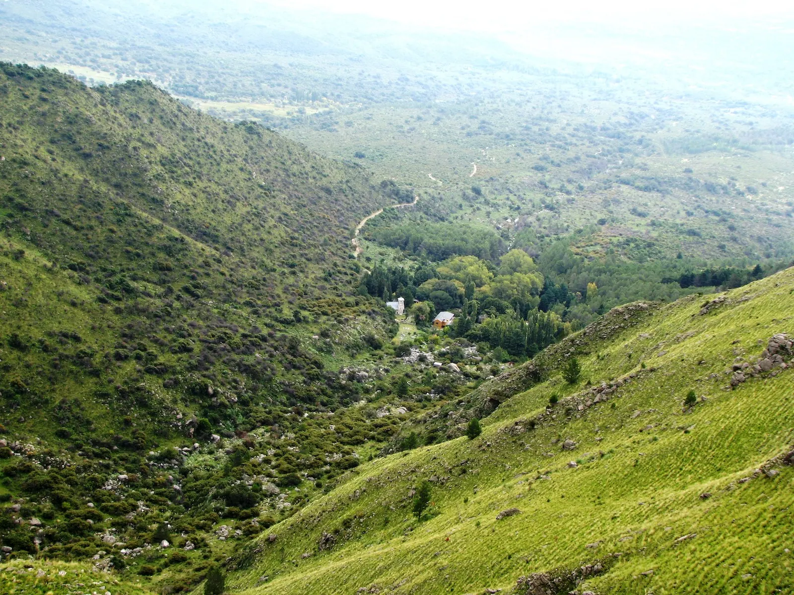 La quebrada verde vista desde arriba, con la casa entre los árboles del fondo.