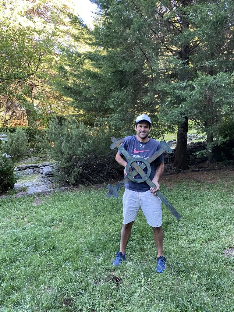 Una persona sosteniendo con las dos manos una cruz de hierro en el parque.
