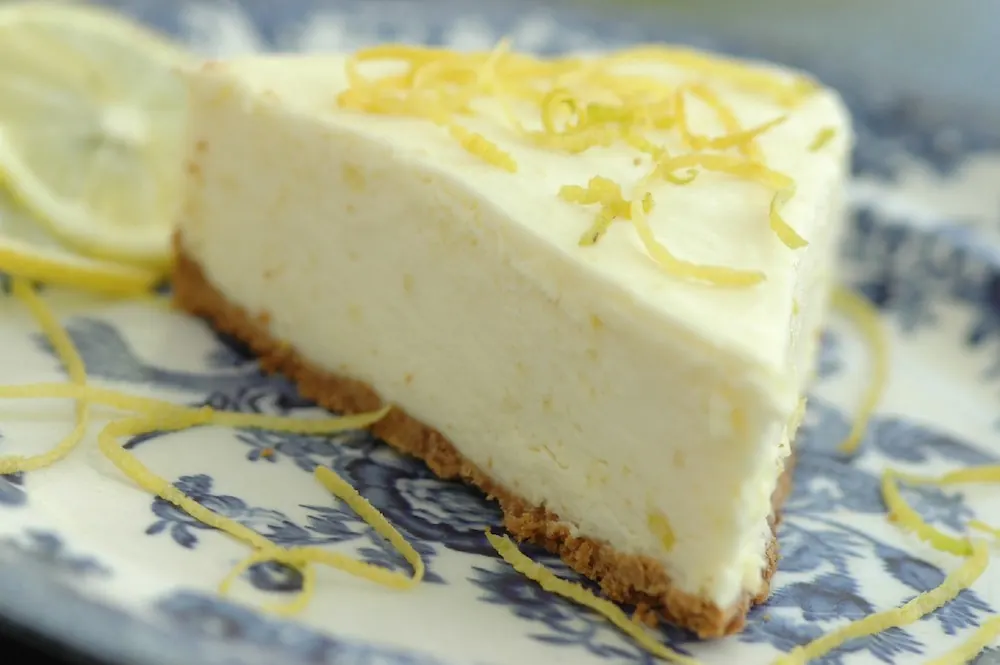 Una porción de cheesecake de limón en un plato de loza azul.