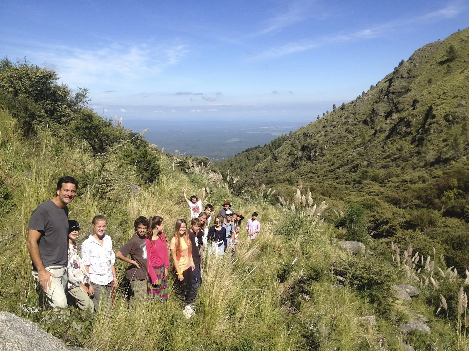 Chicos y un adulto subiendo por un sendero entre pastizal, con las sierras y el llano detrás.
