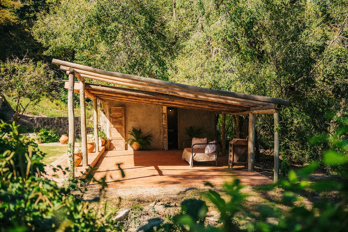 Un rancho de madera con techo de paja y dos sillones en el deck, entre los árboles.