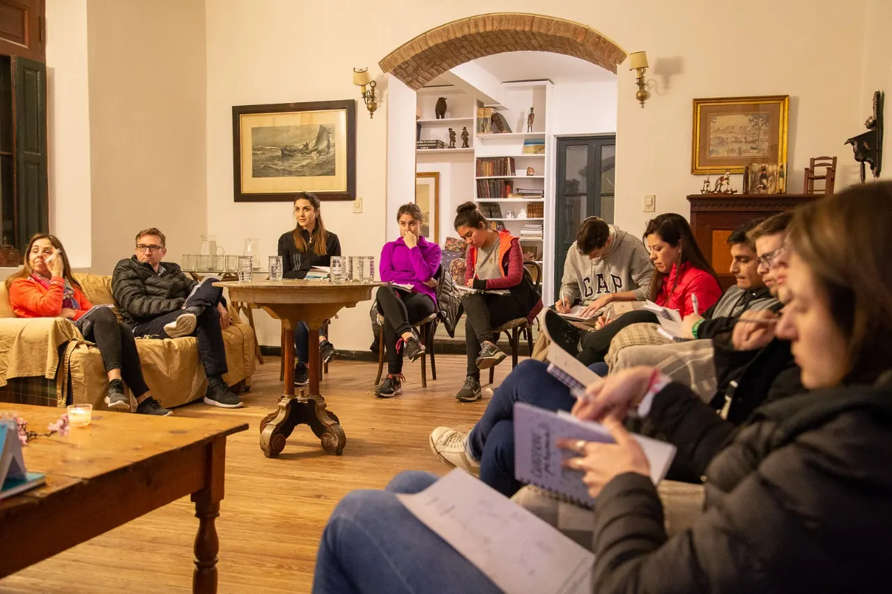 Gente leyendo y conversando en el living, de noche.