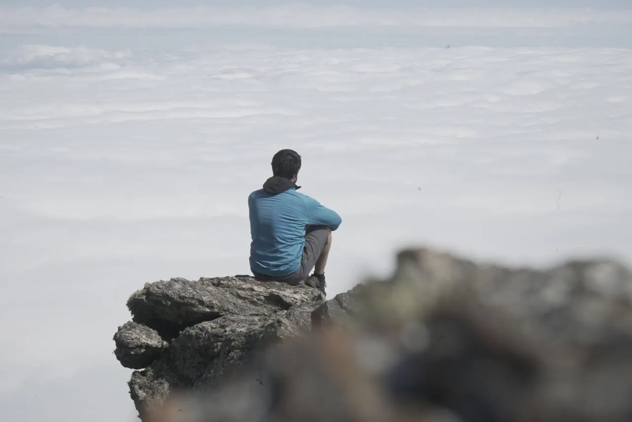Una persona sentada en el borde de una roca, mirando el mar de nubes desde la altura.
