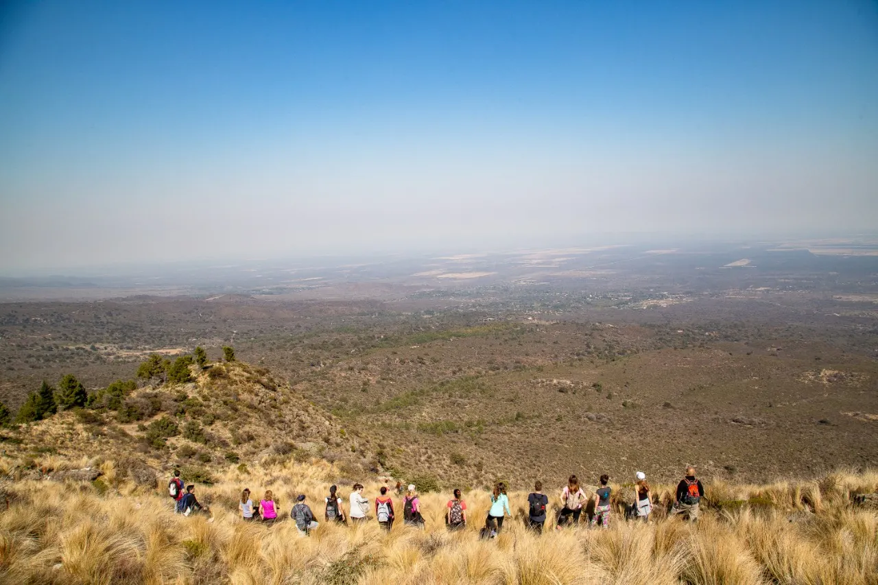 Una fila de caminantes cruzando el filo, con el llano al fondo.