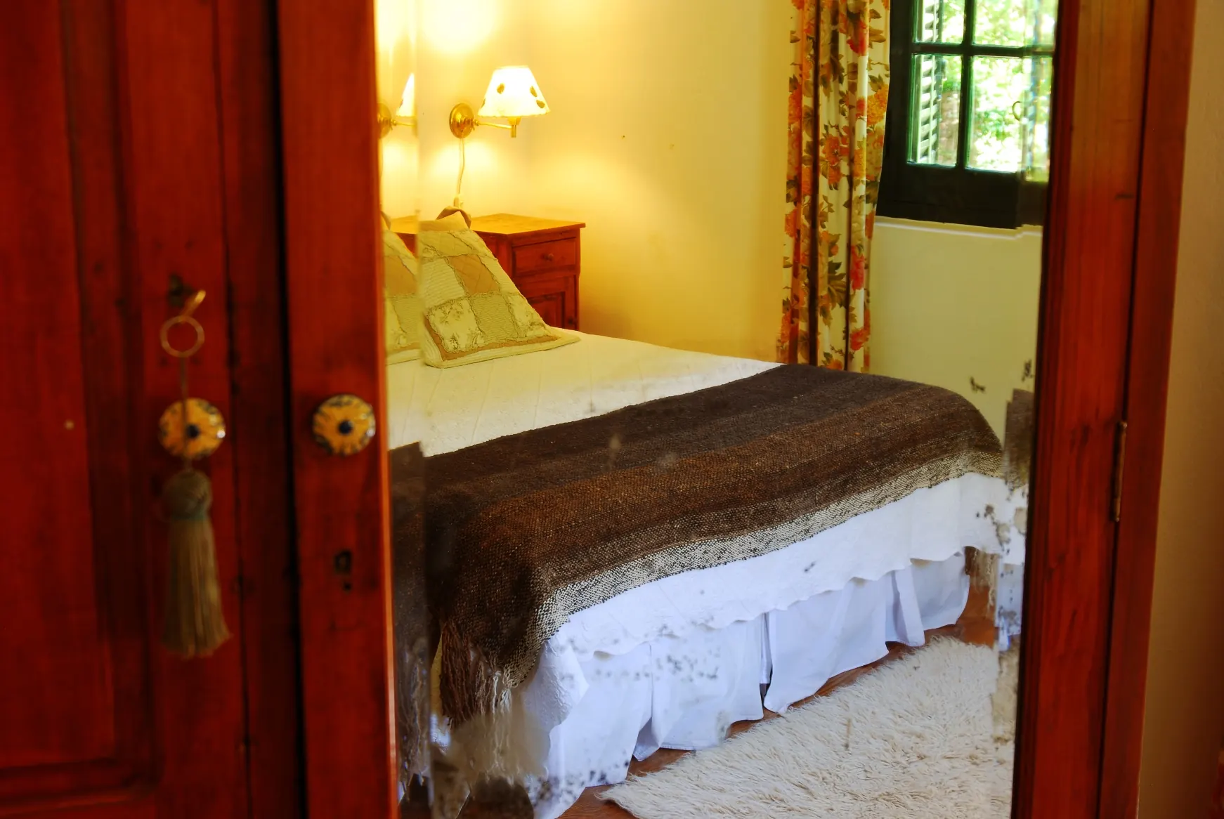 Un dormitorio visto desde la puerta de madera, con la cama tendida y una manta marrón.