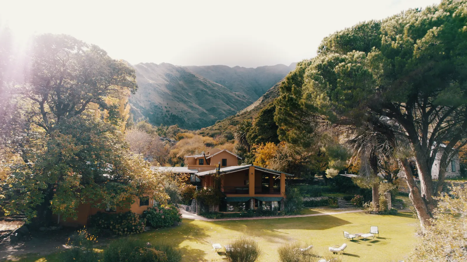 La casa en el fondo del valle a contraluz, con el sol filtrándose entre los árboles.