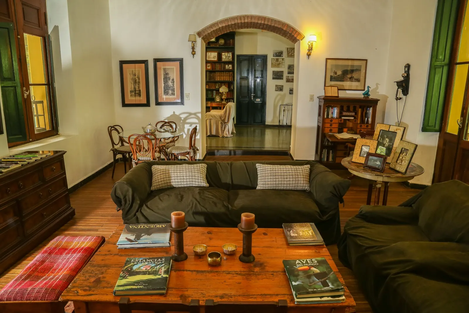 El living de la casa vieja con sofás verdes, biblioteca y cuadros.