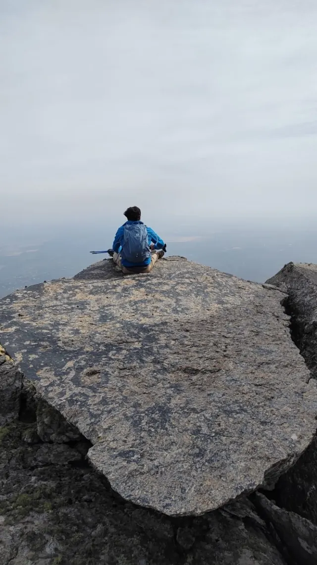 Una persona sentada y quieta en el borde de una laja de granito, mirando el vacío.