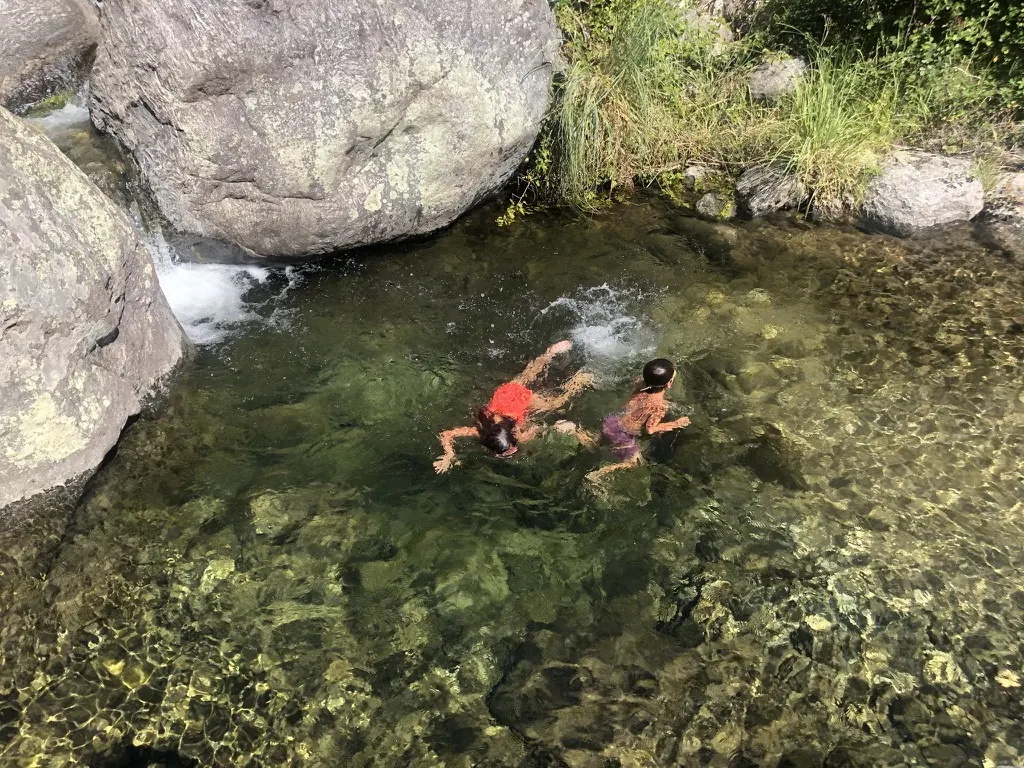 Dos chicos nadando en una olla del arroyo, con el agua transparente sobre las piedras.