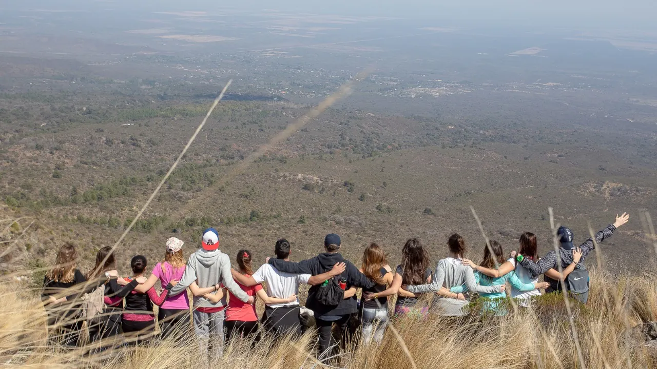 Un grupo abrazado, de espaldas y en fila sobre el pastizal del filo, mirando el llano de Traslasierra.