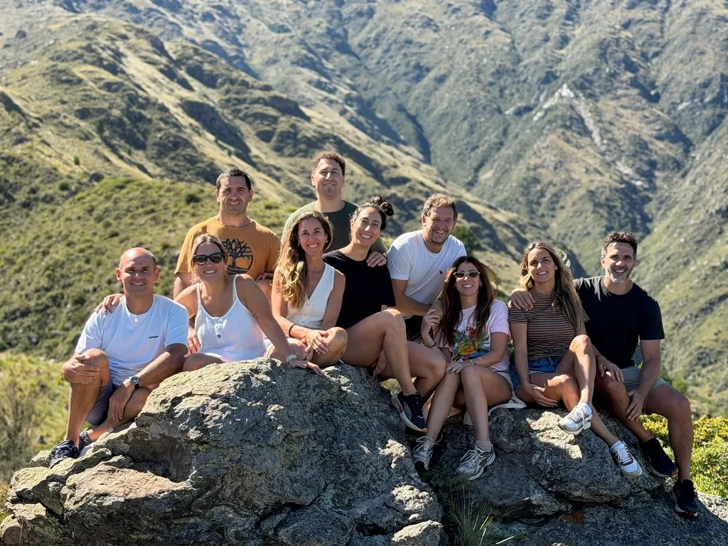 Diez amigos sentados sobre una roca en la ladera, con las sierras verdes detrás.