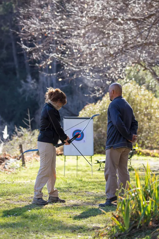 Una persona apuntando con un arco al blanco en el parque, con el instructor al lado.