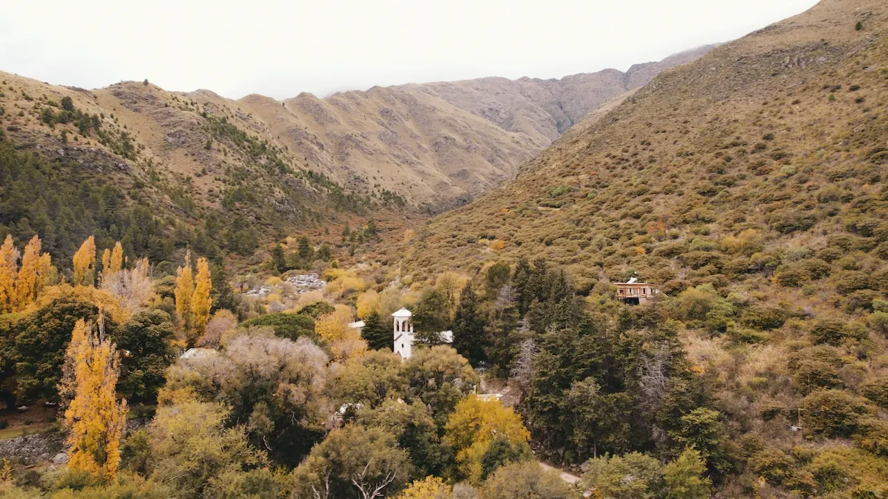 Vista aérea de la casa entre álamos amarillos, en el fondo de la quebrada, en otoño.