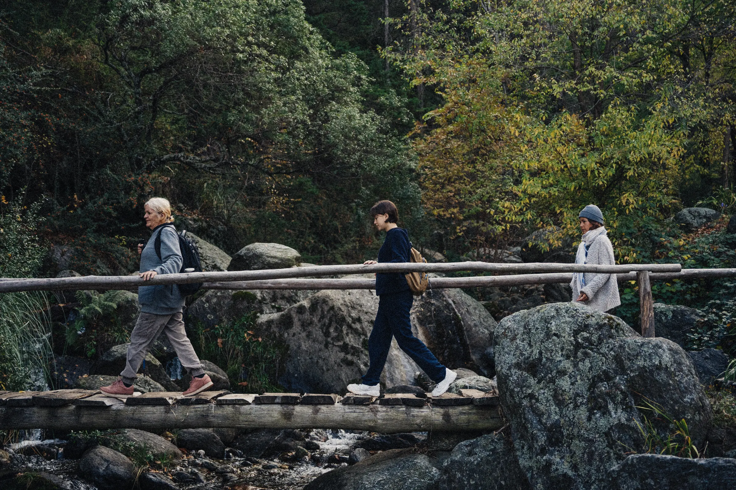 Tres personas cruzando el puente de troncos sobre el arroyo.