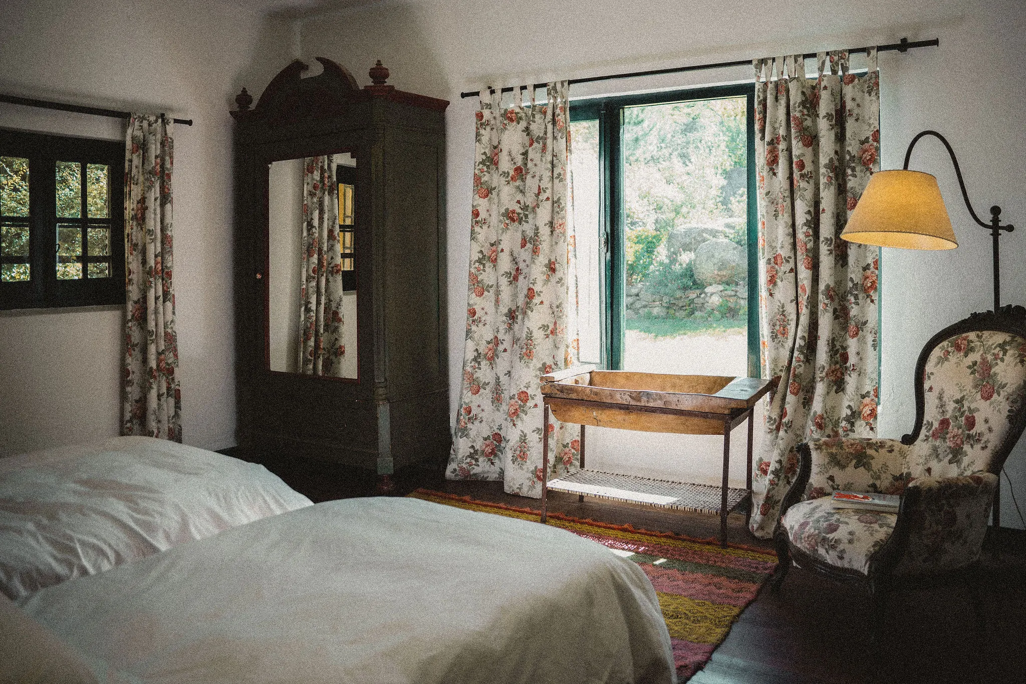 Dormitorio con cortinas floreadas, ropero antiguo y ventana al parque.