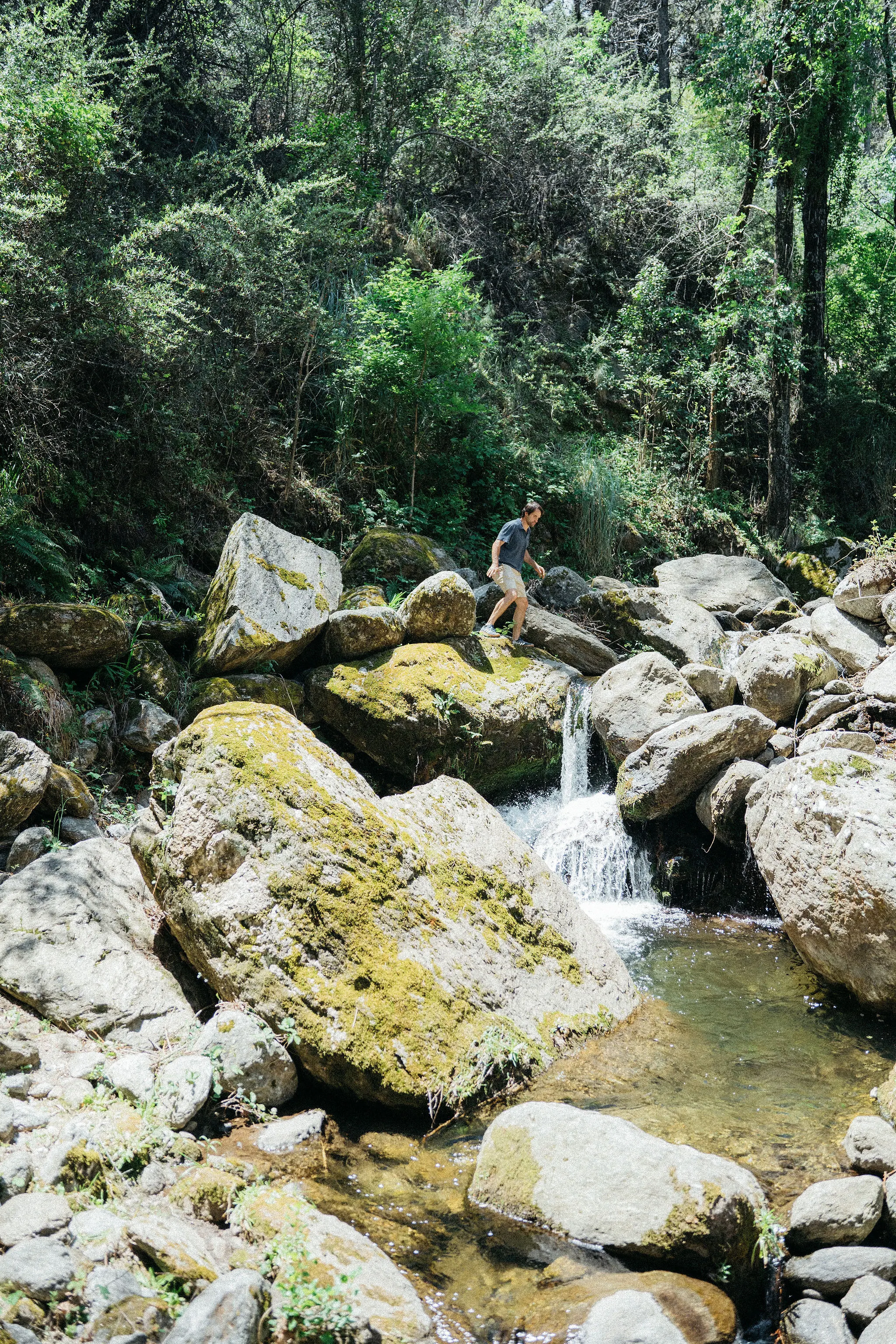 Una persona sentada sobre las rocas, entre los saltos del arroyo.