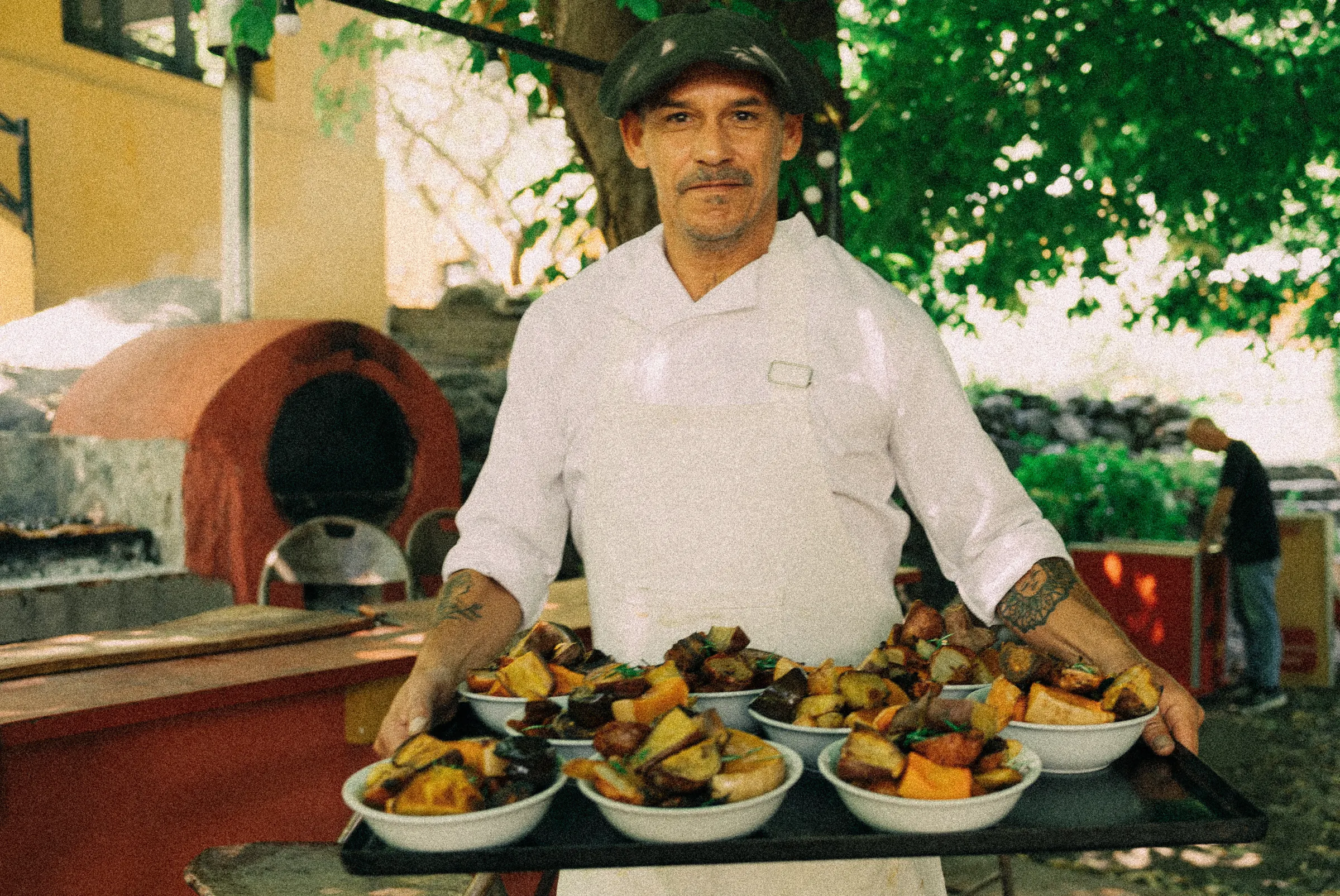 El cocinero saliendo del horno con una bandeja de platos servidos.