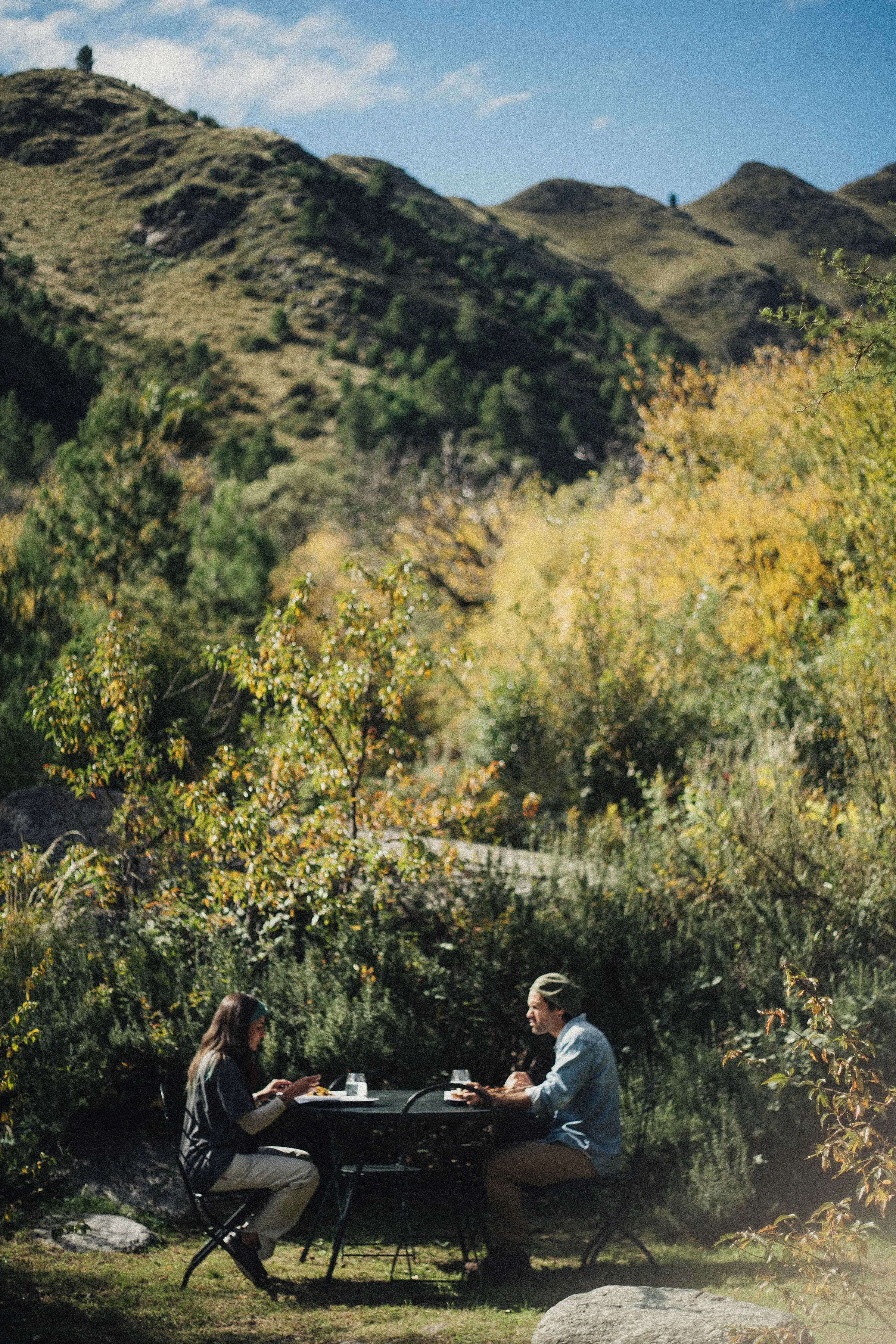 Una pareja desayunando en una mesita afuera, con la sierra al fondo.