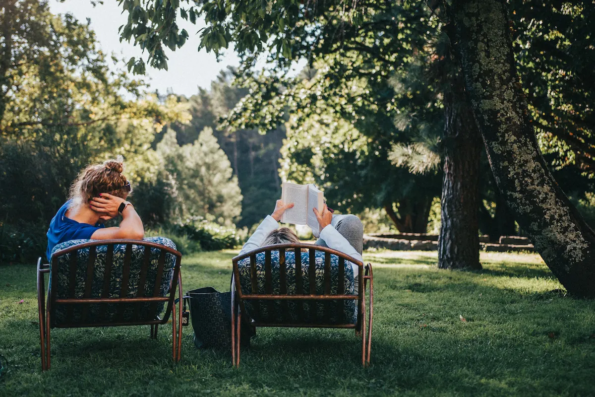 Dos personas leyendo en reposeras, a la sombra del parque.