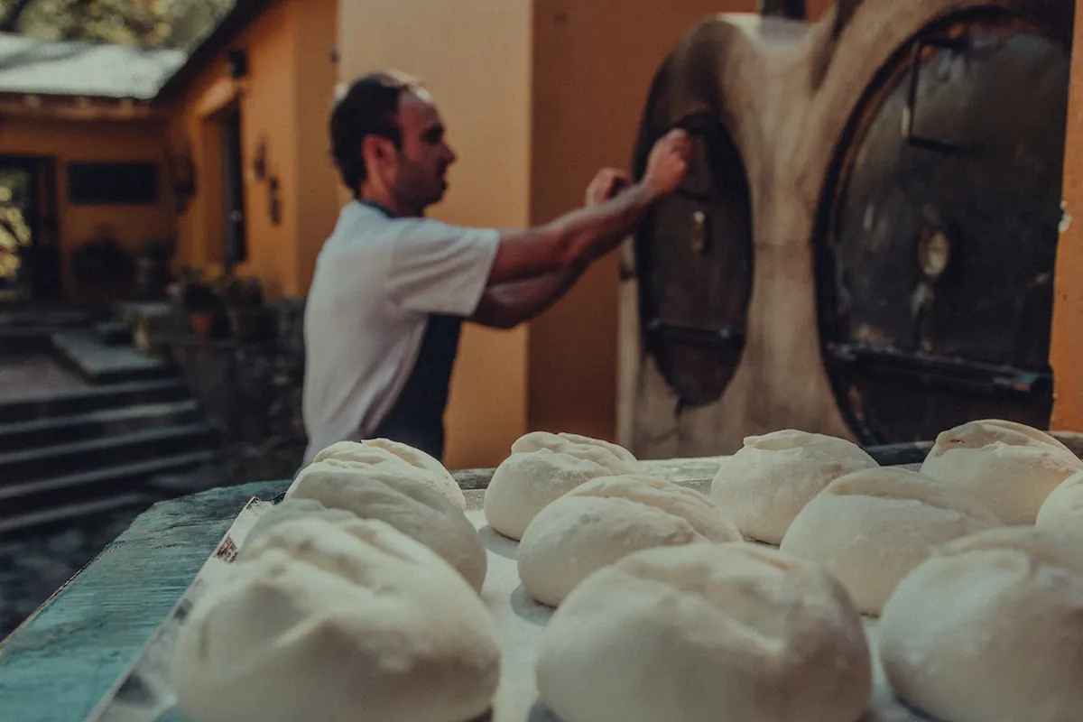 El panadero cargando el horno, con los bollos de masa en primer plano.