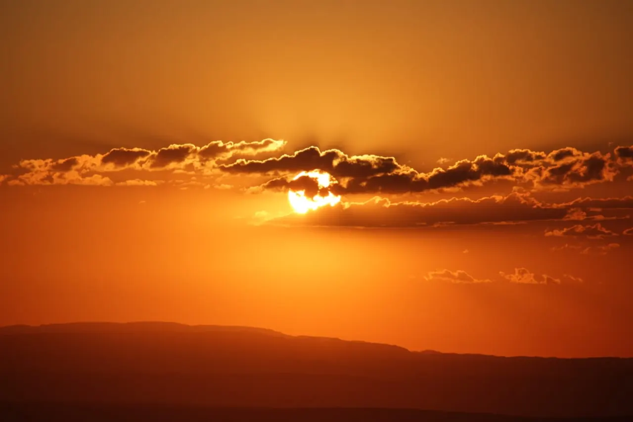 Atardecer naranja con el sol entre nubes, sobre el perfil de la sierra.
