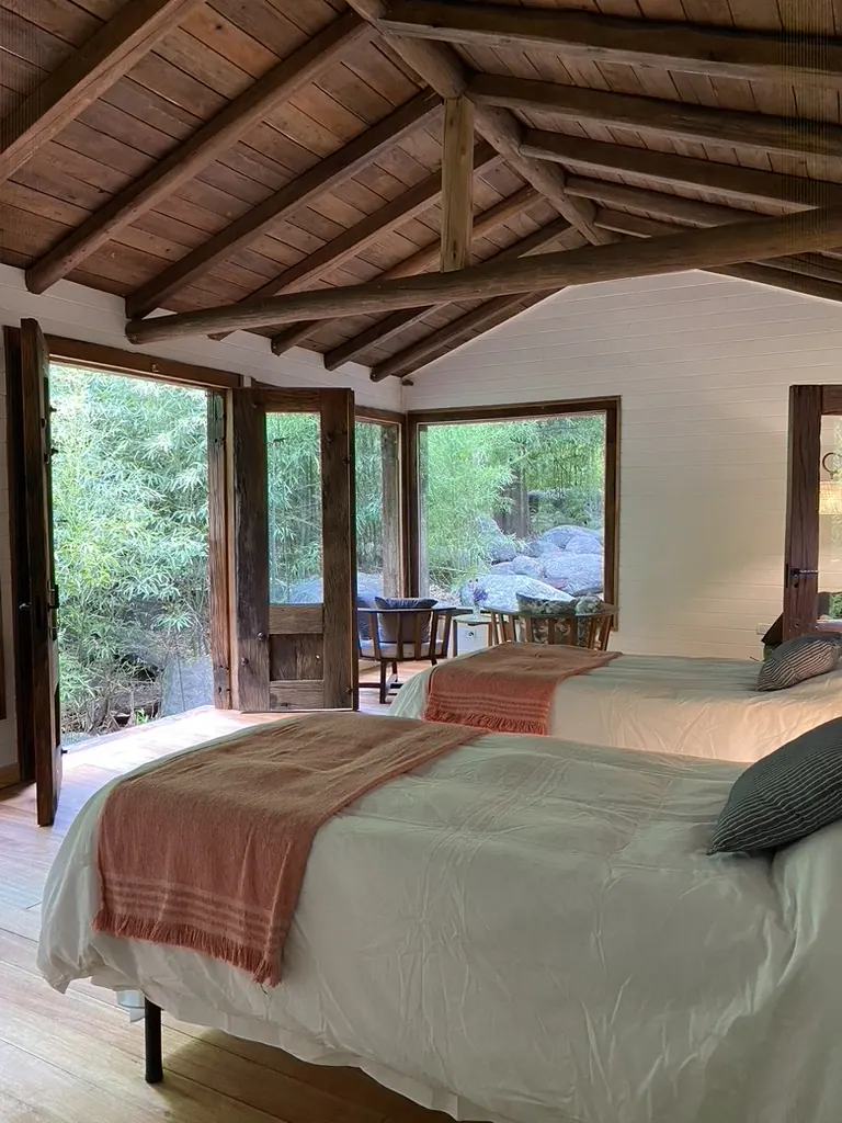 Interior de madera con techo de tirantes a la vista, dos camas y puertas vidriadas al deck.