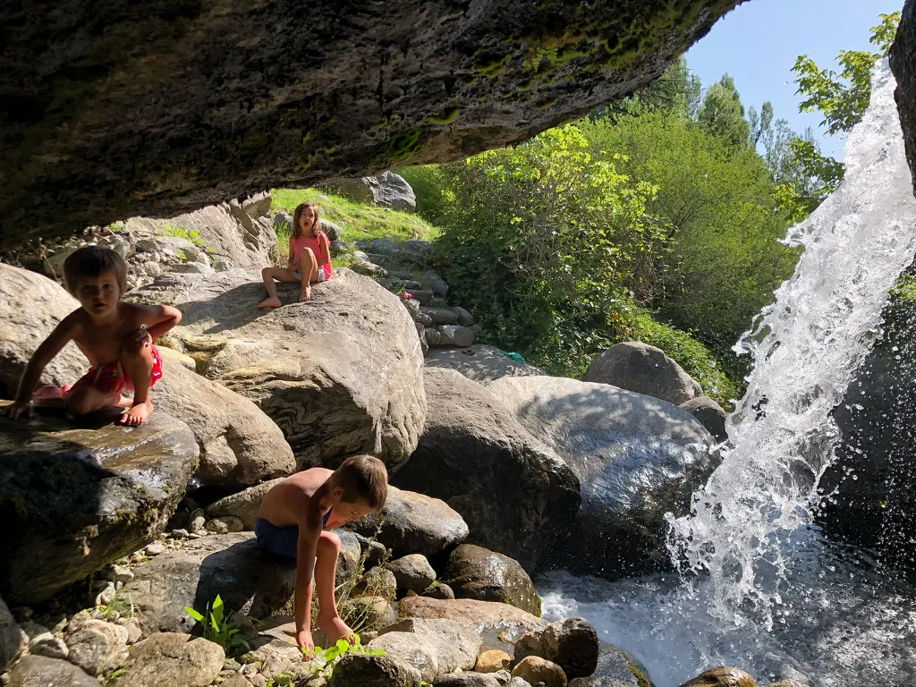 Tres chicos en malla jugando sobre las rocas bajo un peñasco, al lado del chorro de la cascada.