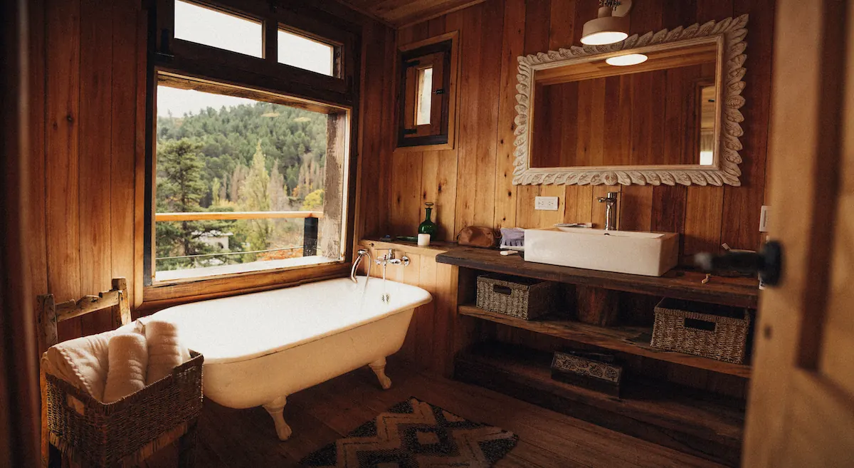 Un baño de madera con bañadera con patas y ventana al bosque.