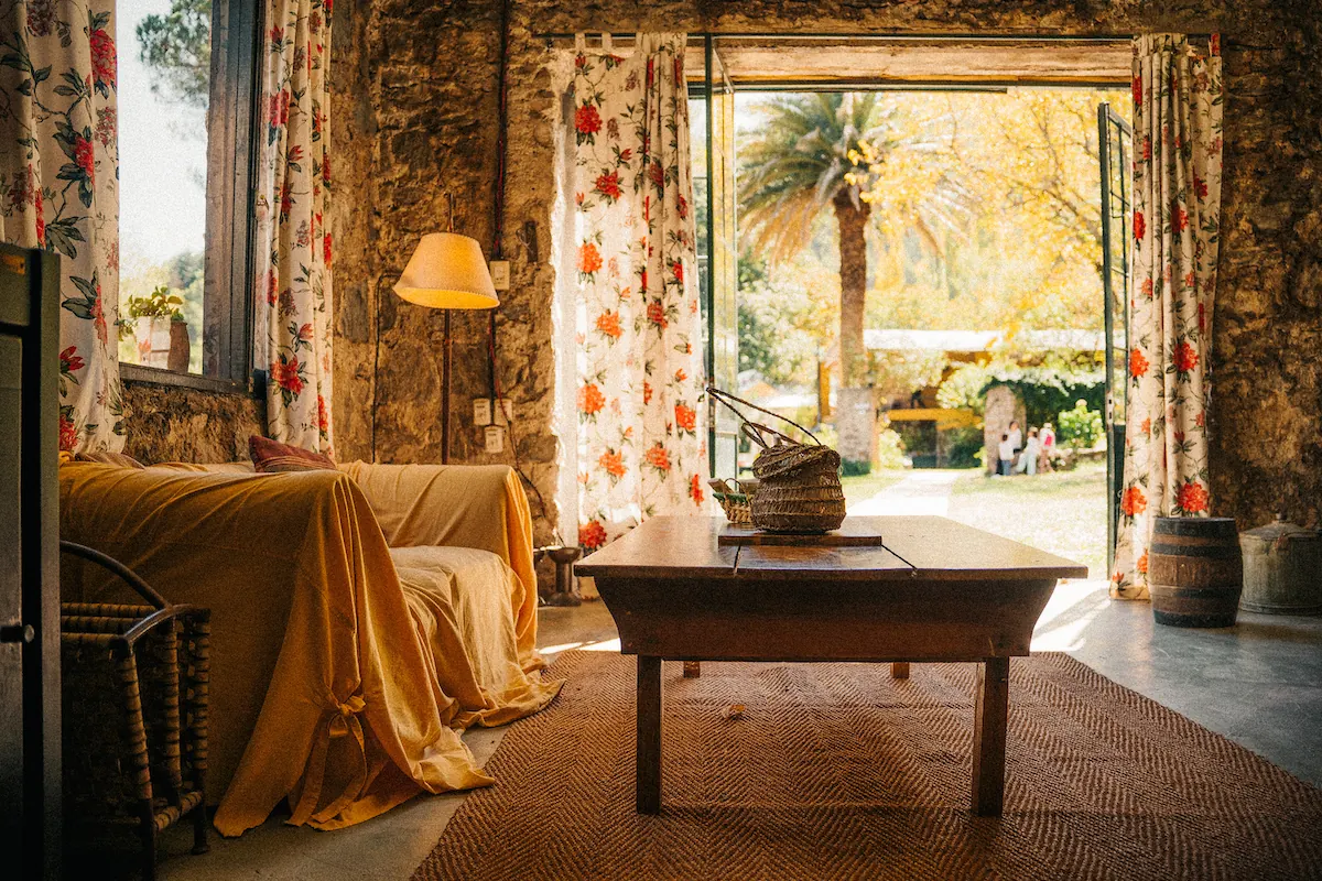 Un living con sillón amarillo, cortinas floreadas y la puerta abierta al parque.