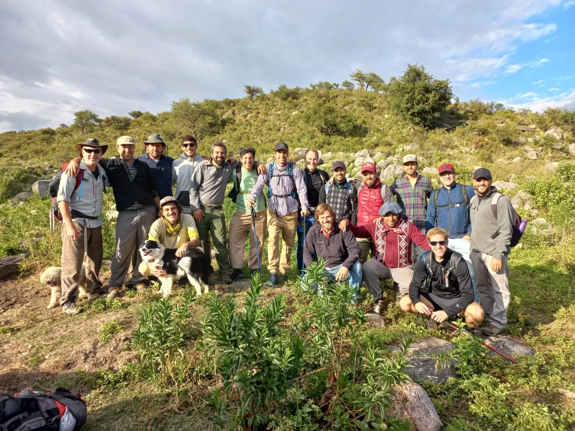 Un grupo de unos veinte caminantes con mochilas, subiendo por el pastizal de altura.