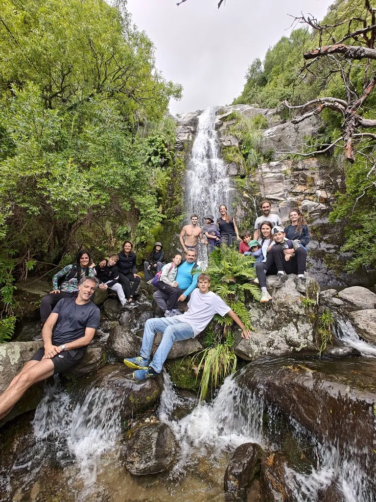 Una familia grande, chicos y grandes, sentados en las rocas al pie de la cascada, entre helechos.