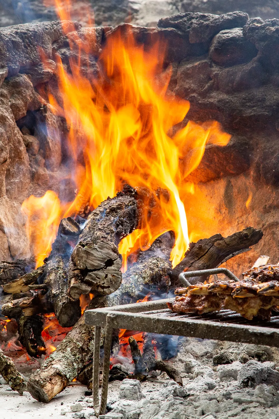 Las llamas de la leña detrás de la parrilla de hierro, con un costillar asándose.