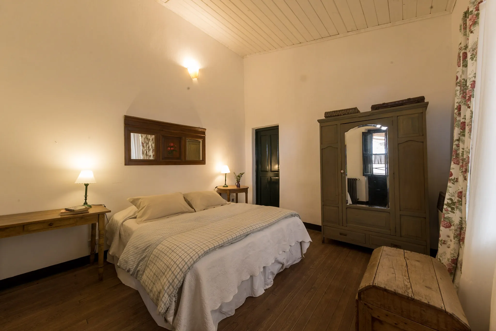 Habitación con cama matrimonial, ropero de madera y mesa larga bajo el espejo.