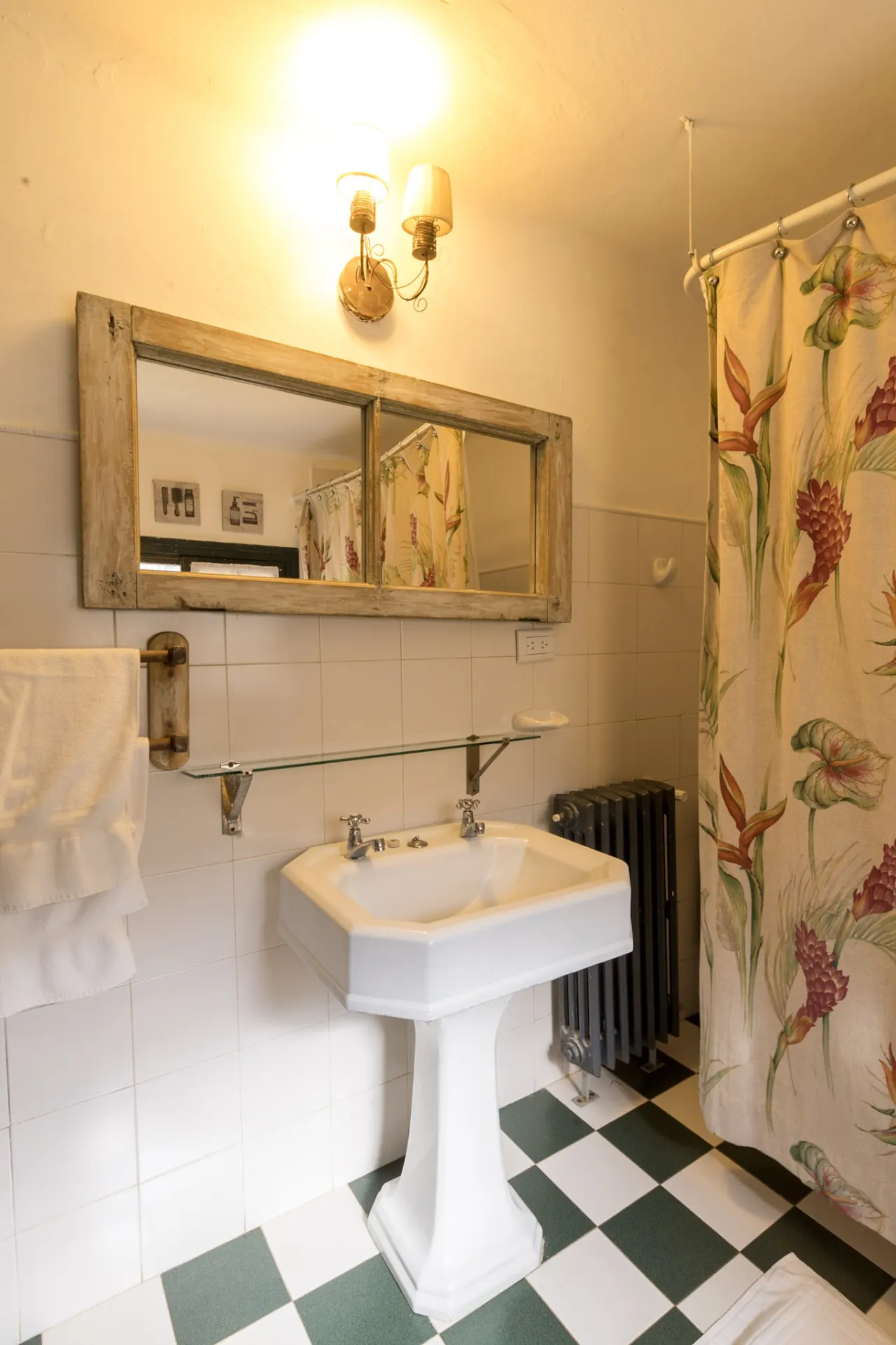 Baño con lavatorio de pie, espejo de madera y piso ajedrezado.