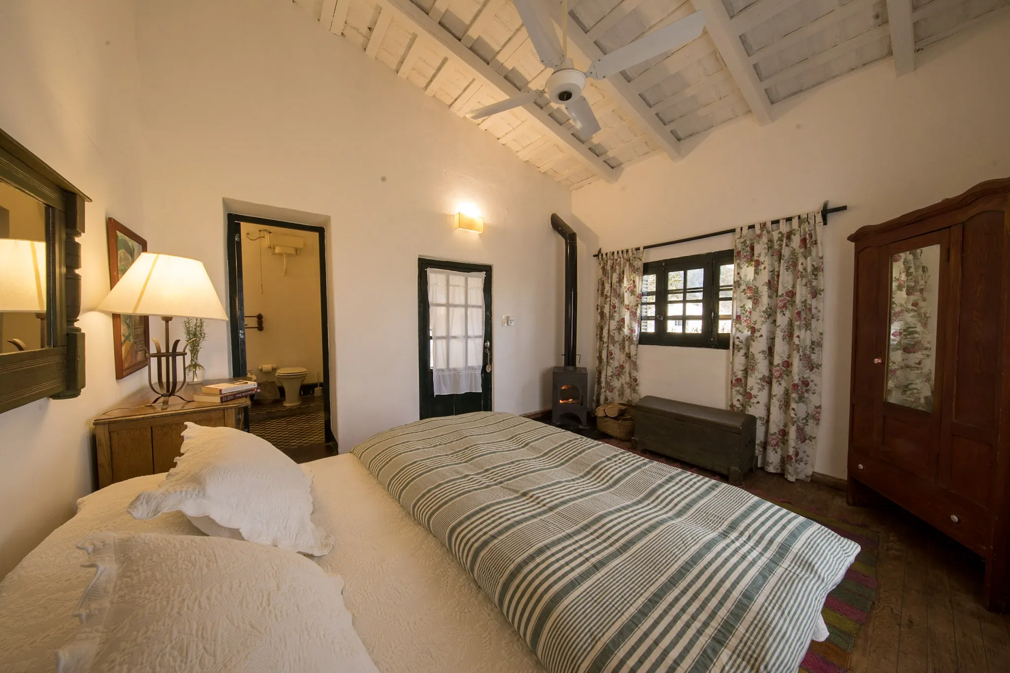 La habitación desde el otro extremo, con la cama contra la pared y las puertas de madera.