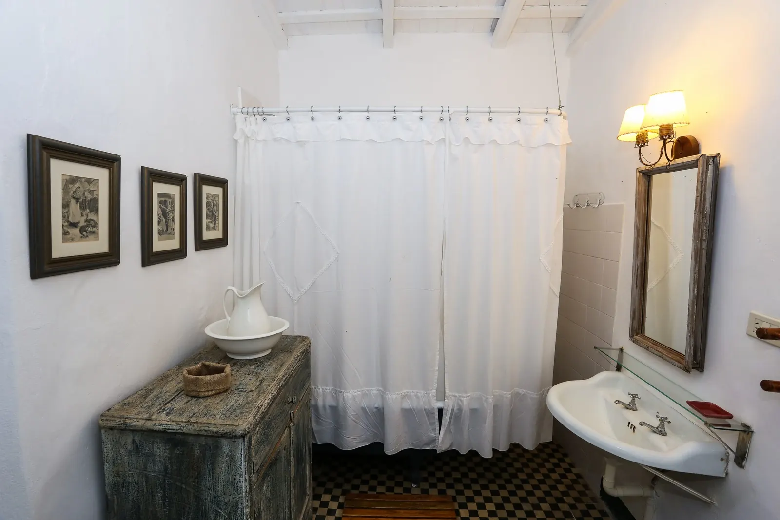 Baño con cortina blanca, lavatorio y mueble de madera desgastada.
