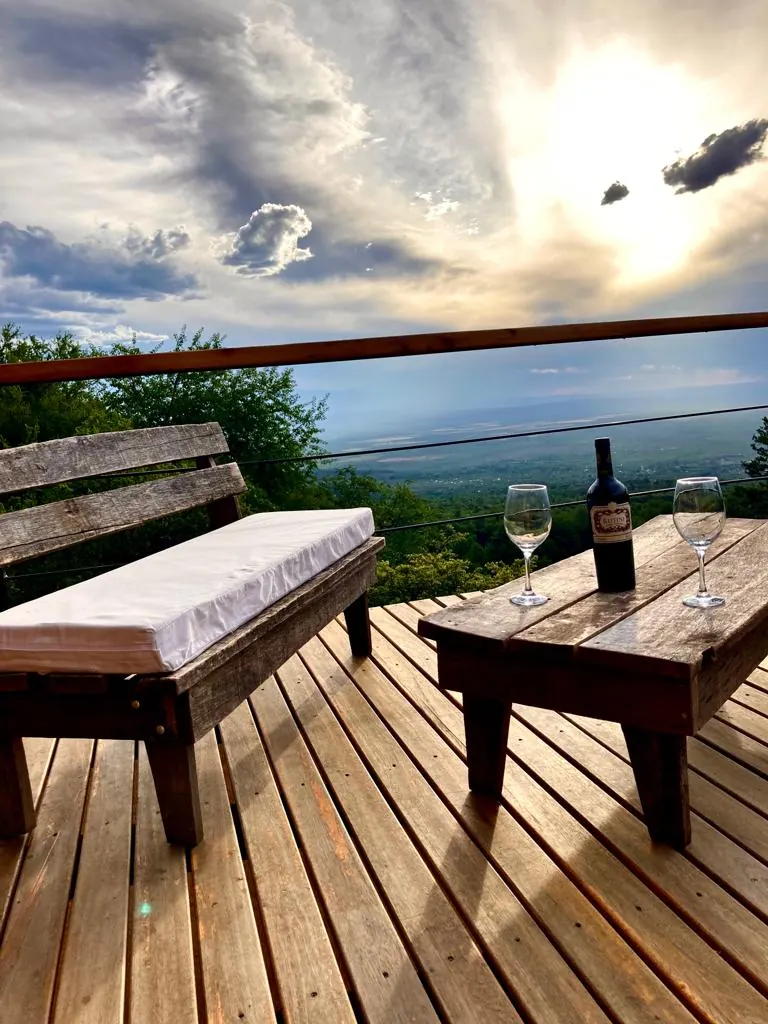 El deck de madera al atardecer, con un banco, una mesa baja y el valle abajo.