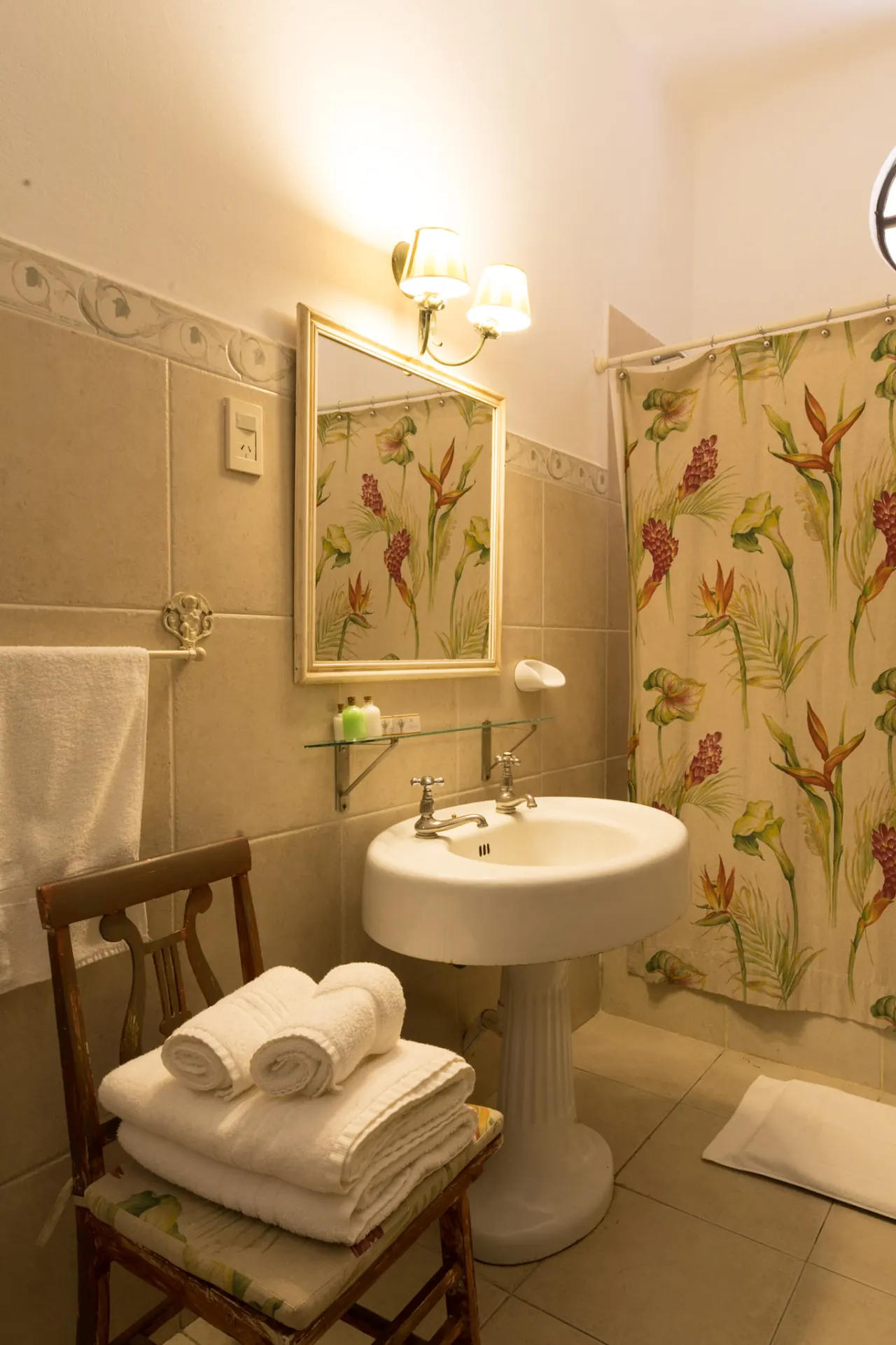 Baño con lavatorio de pie, espejo dorado y las toallas dobladas sobre una silla.