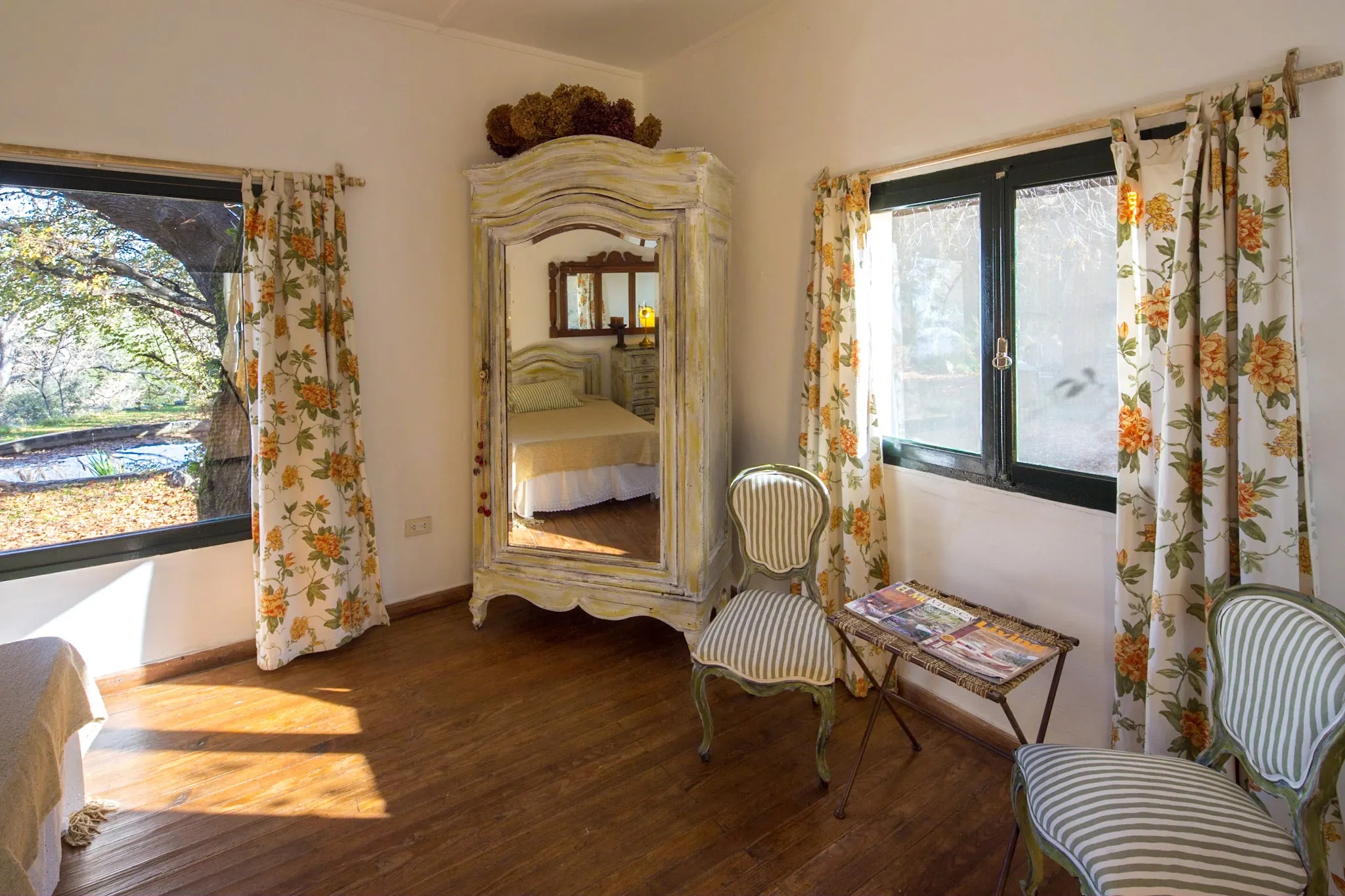 El rincón de la habitación con dos sillones, una mesa baja y el ropero antiguo entre las ventanas.