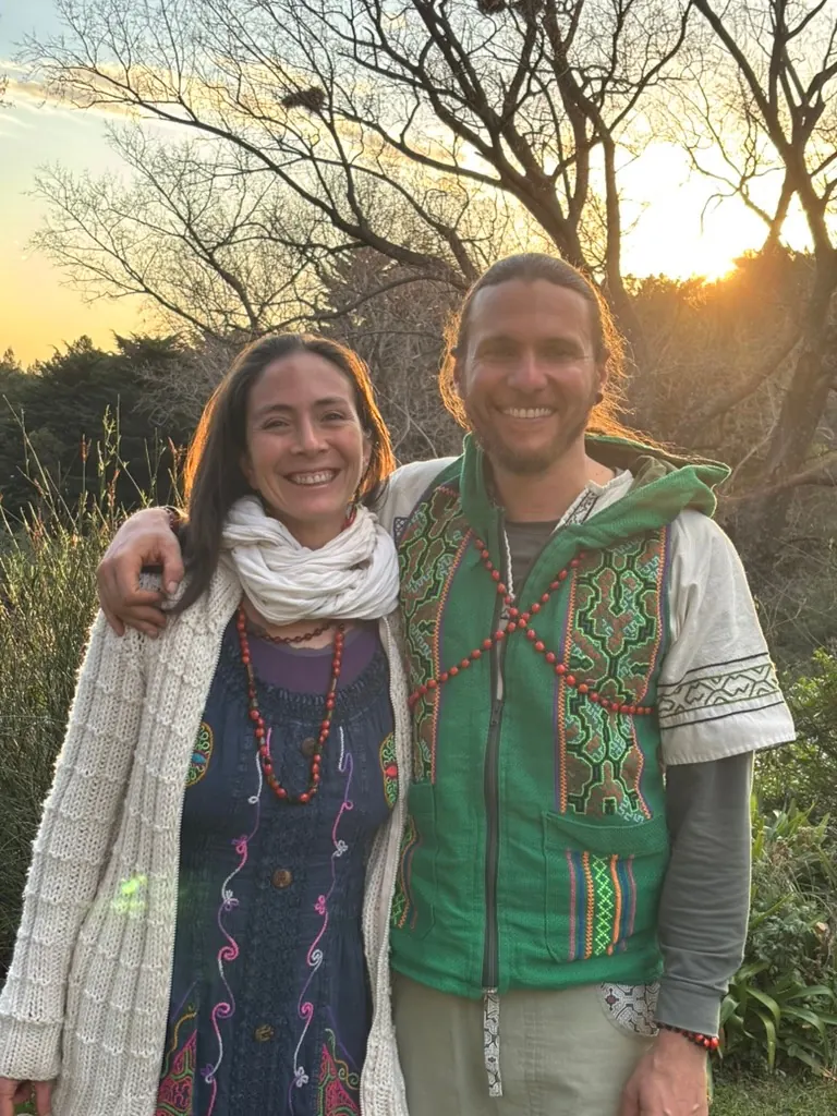 Juan Fezza y Yael Saira abrazados y sonriendo, al atardecer, entre los árboles.