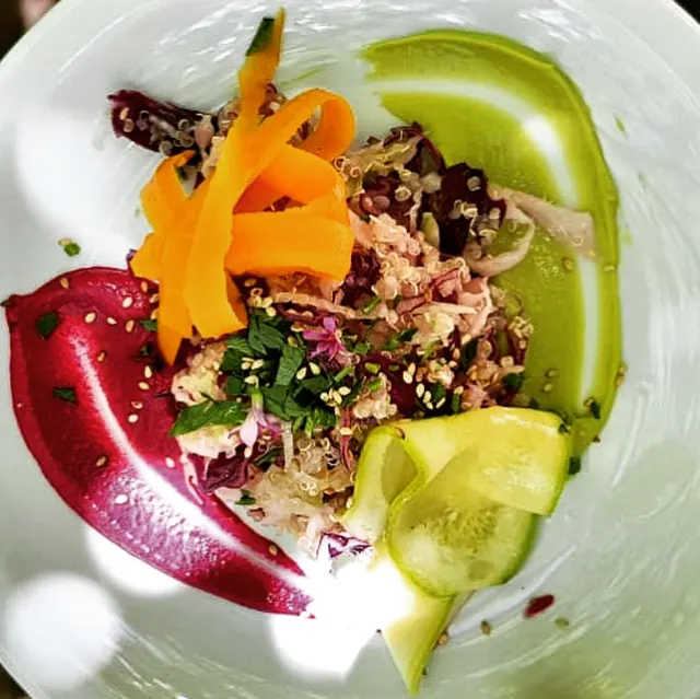 Un plato de quinoa con repollo morado, cintas de zanahoria y pepino, puré de remolacha y crema de palta, visto desde arriba.