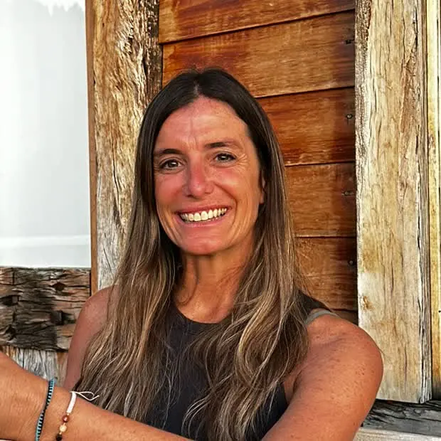 Carmen Burone sentada en una galería de madera, sonriendo, con un mate en las manos.