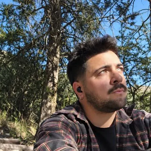 Leo Dietrich sentado sobre una piedra en el monte, mirando hacia arriba, con el cielo despejado detrás.