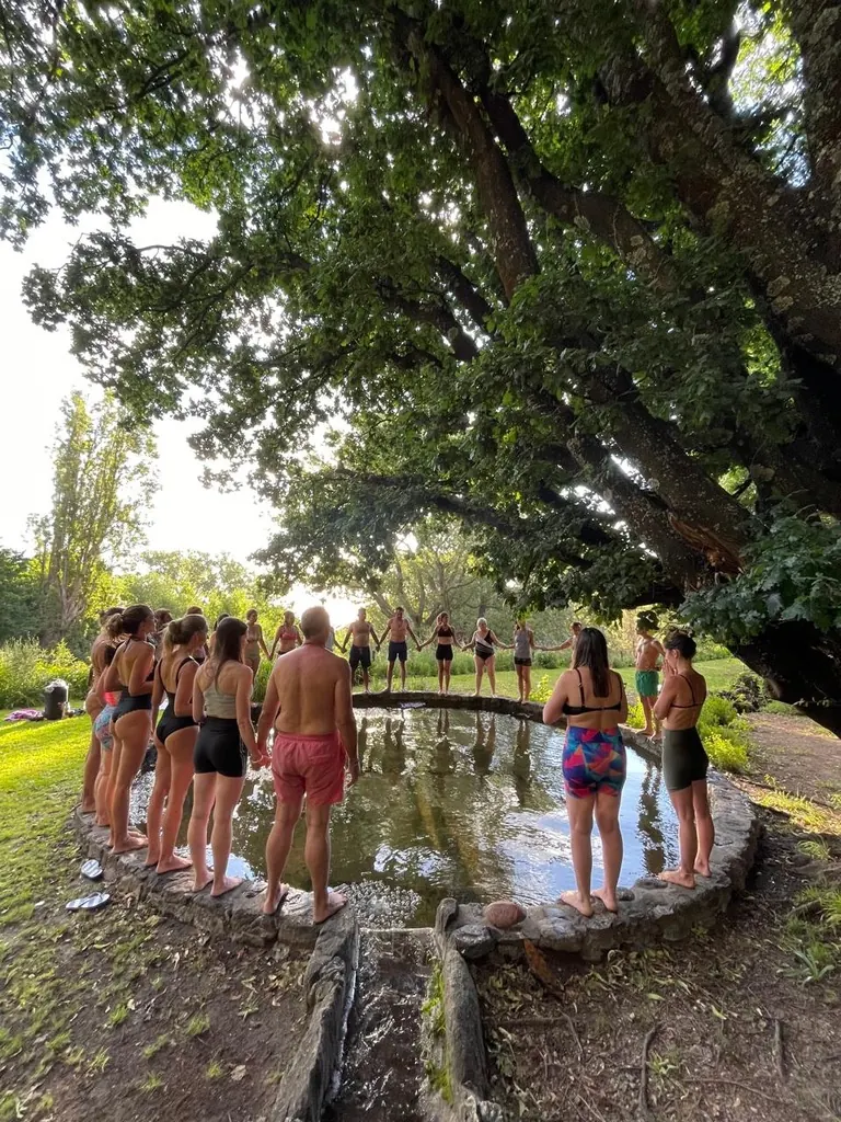 Un grupo en malla tomado de la mano alrededor del estanque de piedra, bajo el roble grande.