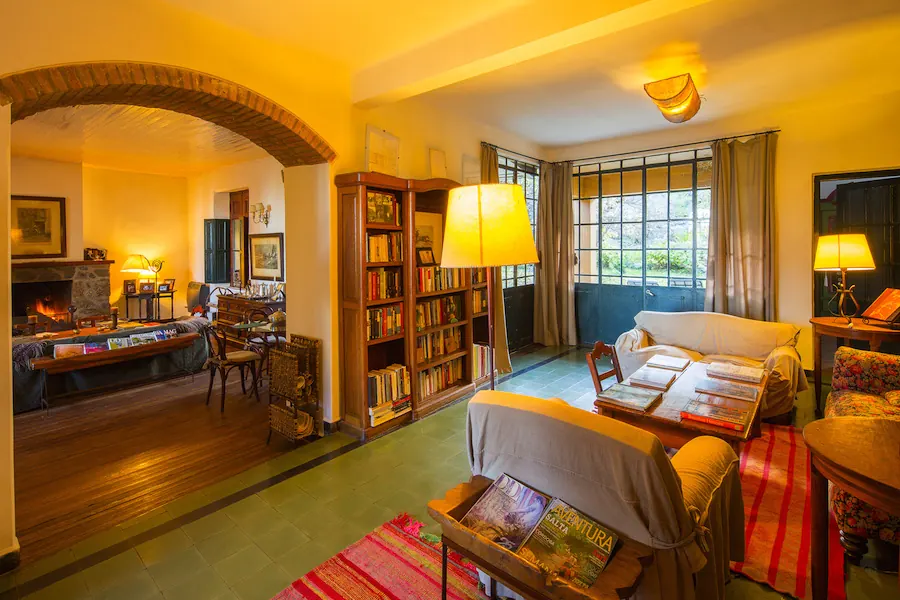 La sala de lectura con dos bibliotecas llenas de libros, sillones, y el arco de ladrillo que da al living con el hogar prendido.