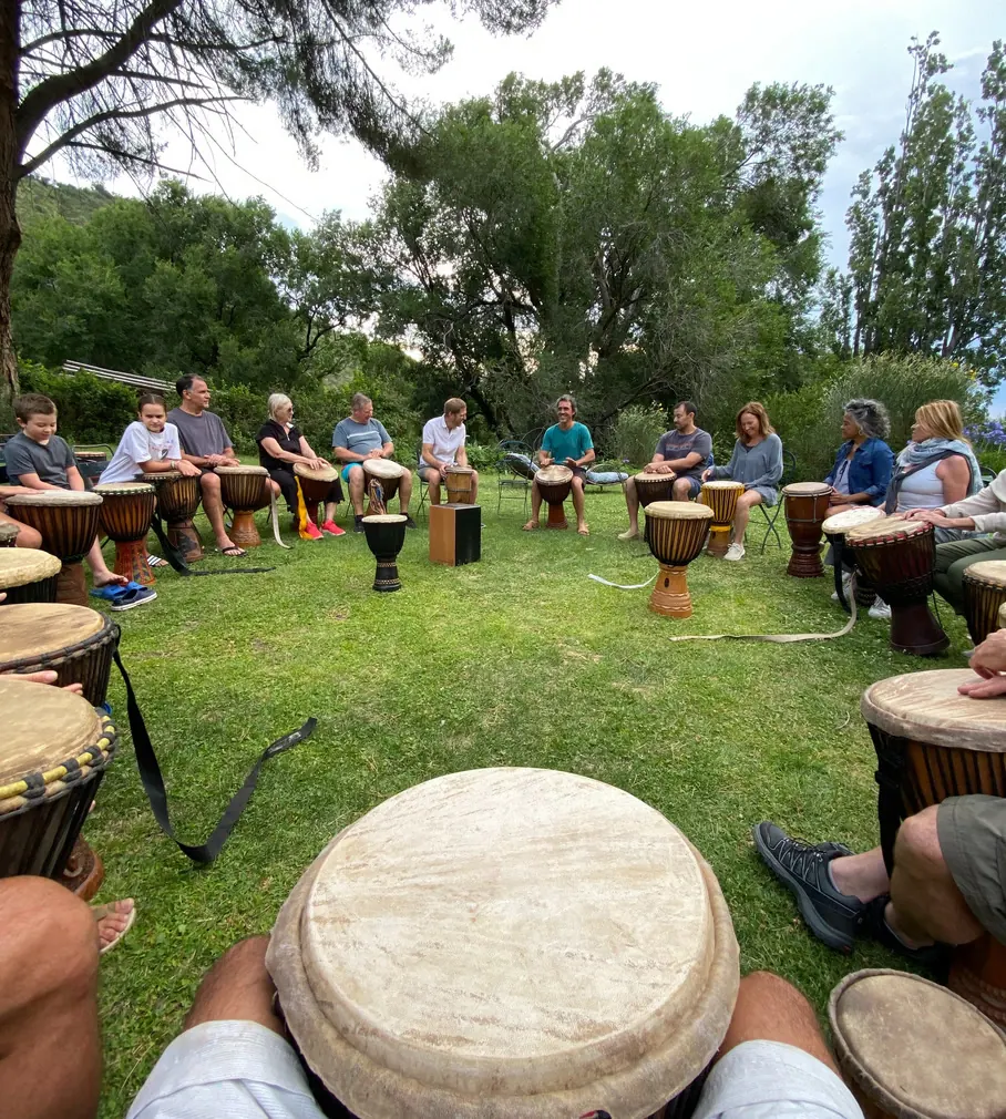 Una ronda de personas de todas las edades tocando tambores sentadas en el jardín, vista desde el lugar de quien toca.